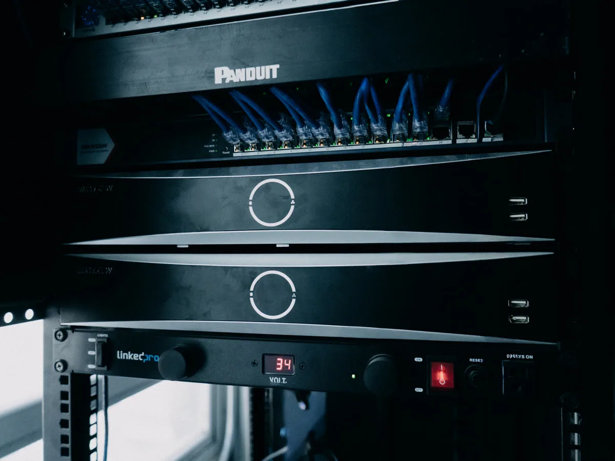 Switch PoE con patch cords azules y grabadores Hikvision en el rack del proyecto